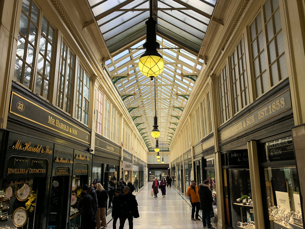 Interior of the Argyll Arcade in Glasgow, showcasing Victorian architecture with a glass roof, ornate shopfronts, and people browsing