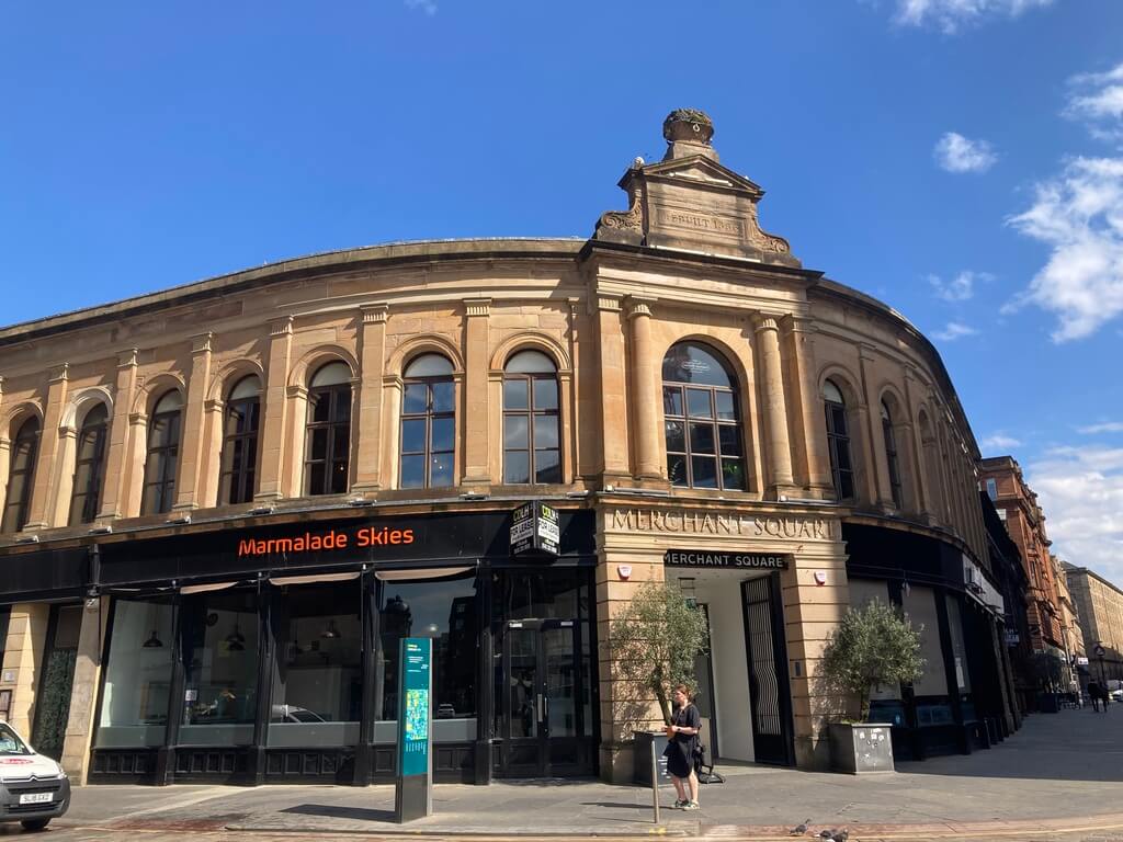 The curved facade of Merchant Square in Glasgow on a sunny day, with a corner café and clear blue skies above