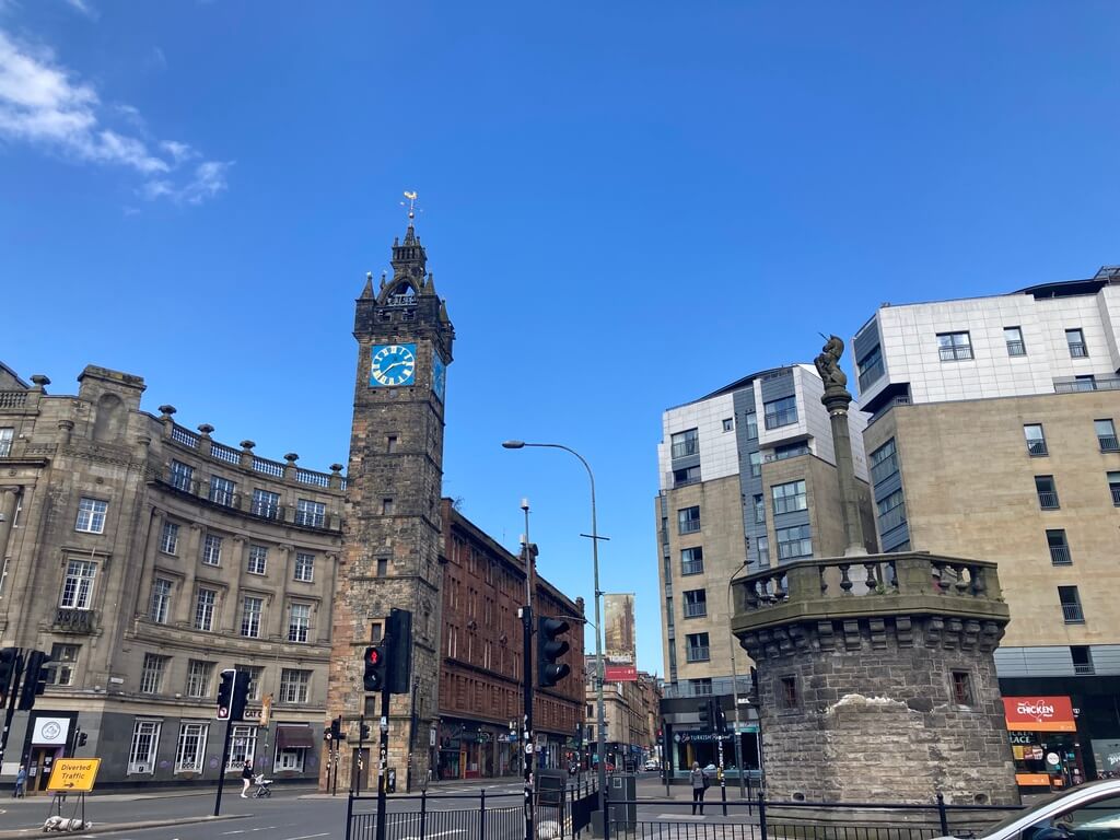 A cityscape view featuring the Tolbooth Steeple, an iconic Glasgow landmark with a clock, set against modern buildings under a clear blue sky